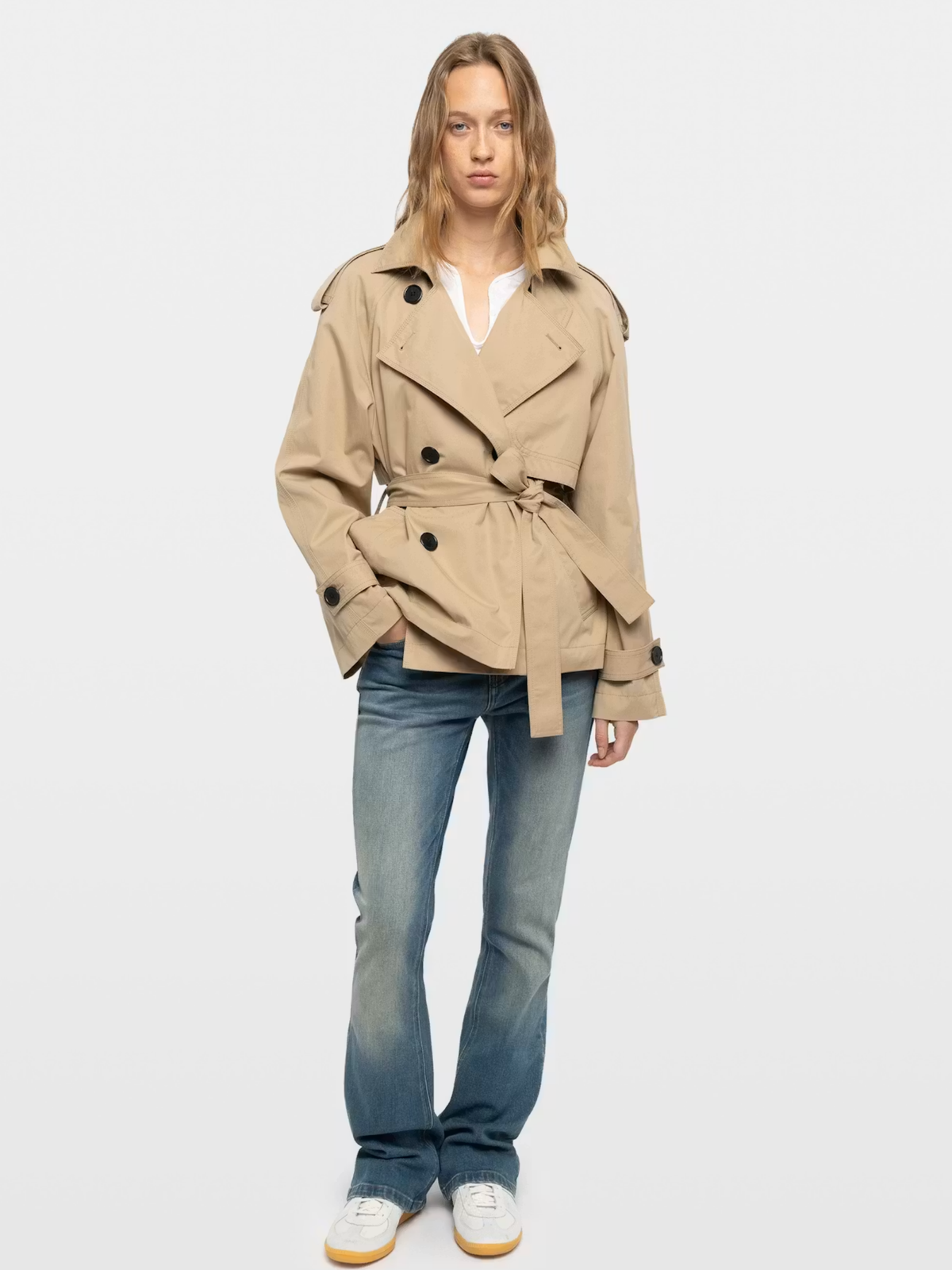 Model wearing a beige belted jacket and jeans for a transitional fall wardrobe